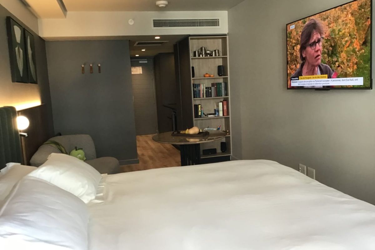 A modern bedroom featuring built-in shelving, ducted air conditioning, and a wall-mounted television, offering a clean and functional living space.