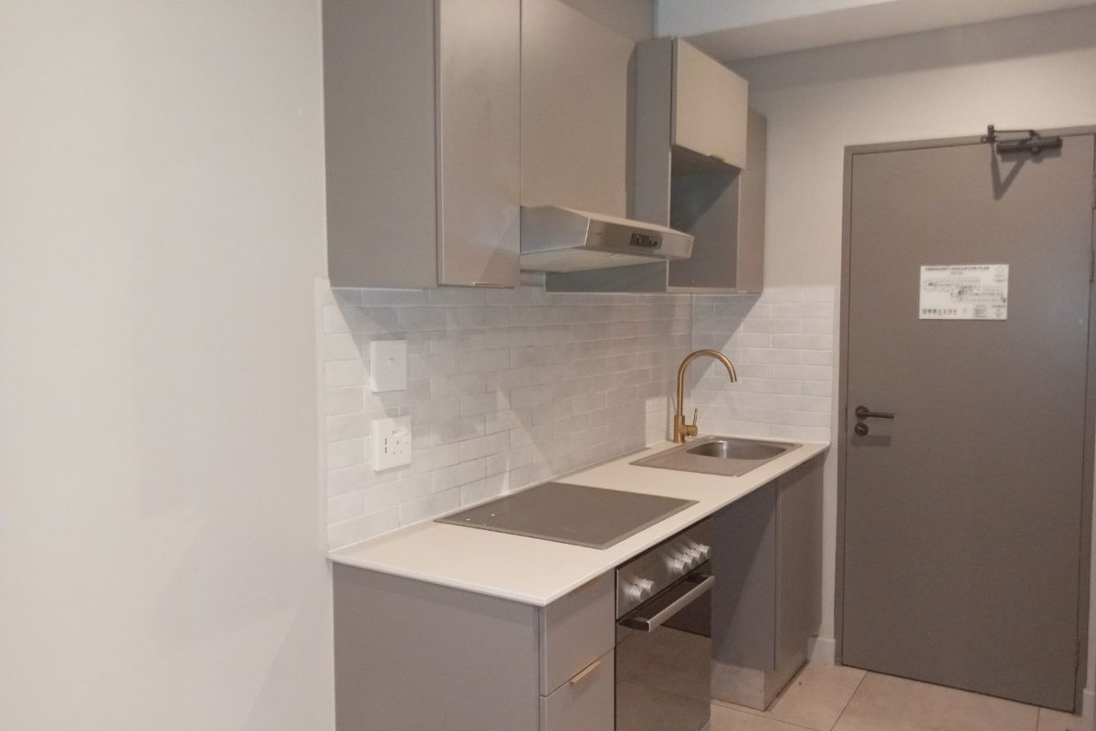 A modern, compact kitchen featuring grey cabinetry, stone countertops, a subway tile backsplash, and integrated appliances including an oven and hob.