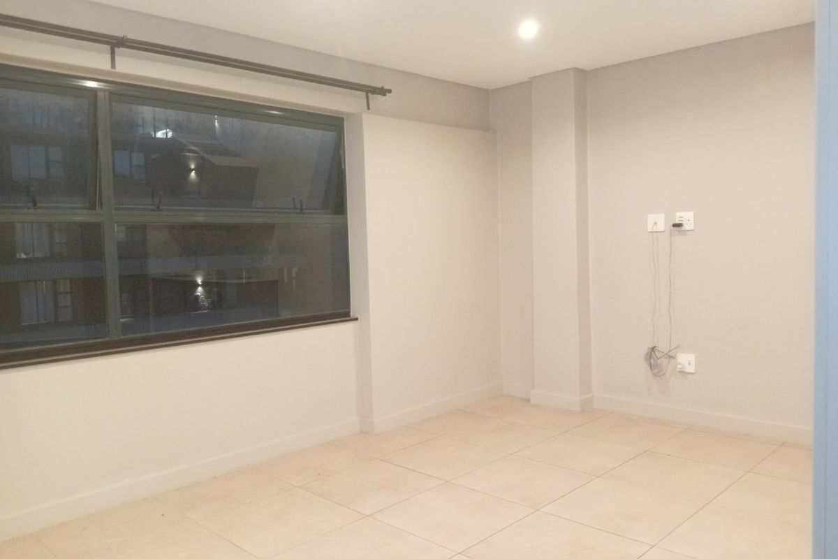 A clean, empty bedroom featuring neutral tiled flooring, recessed downlighting, and a large aluminium-framed window.