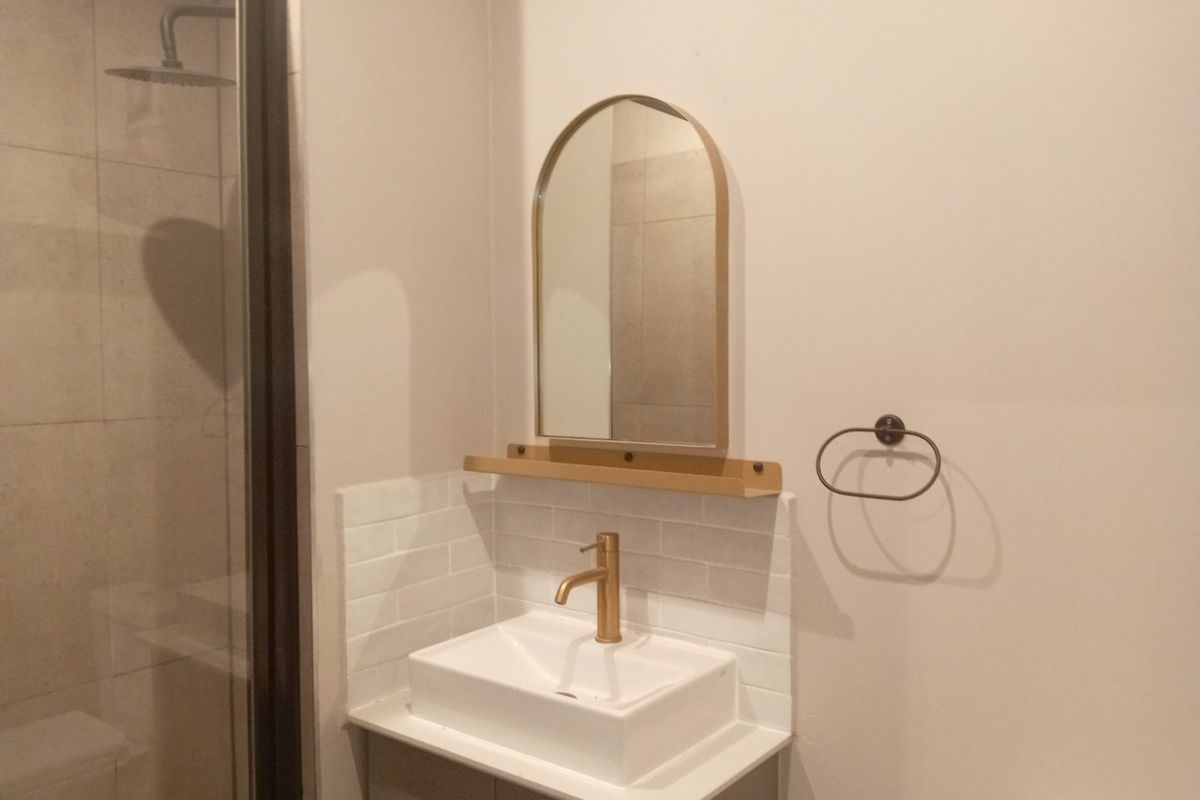Modern bathroom featuring a vanity with a brass faucet, subway tile backsplash, and a glass-enclosed shower with a rain shower head.