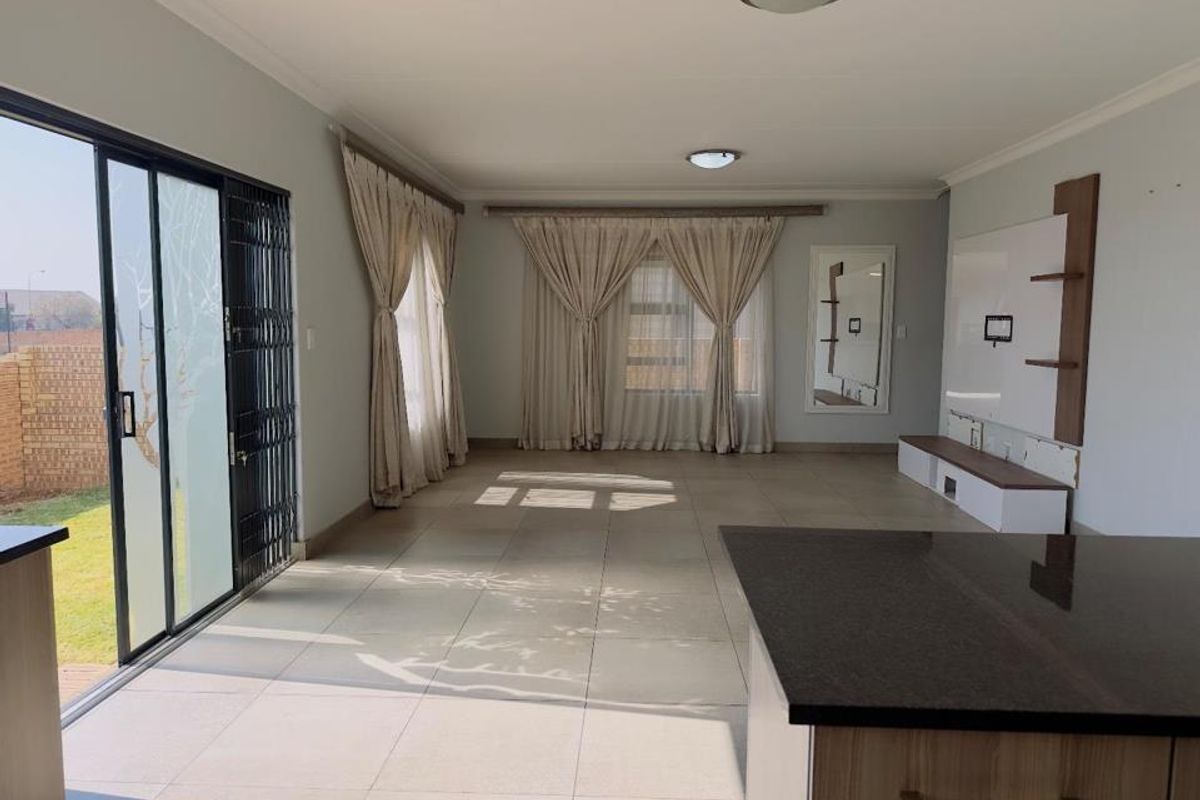 Spacious open-plan living area featuring large tiled floors, a built-in media unit, and sliding glass doors providing direct access to the garden.