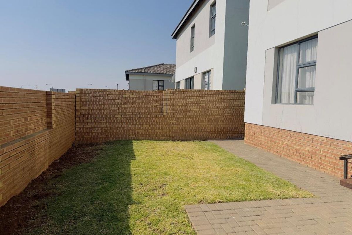 A private rear garden featuring a paved patio area, a small lawn, and secure brick boundary walls.