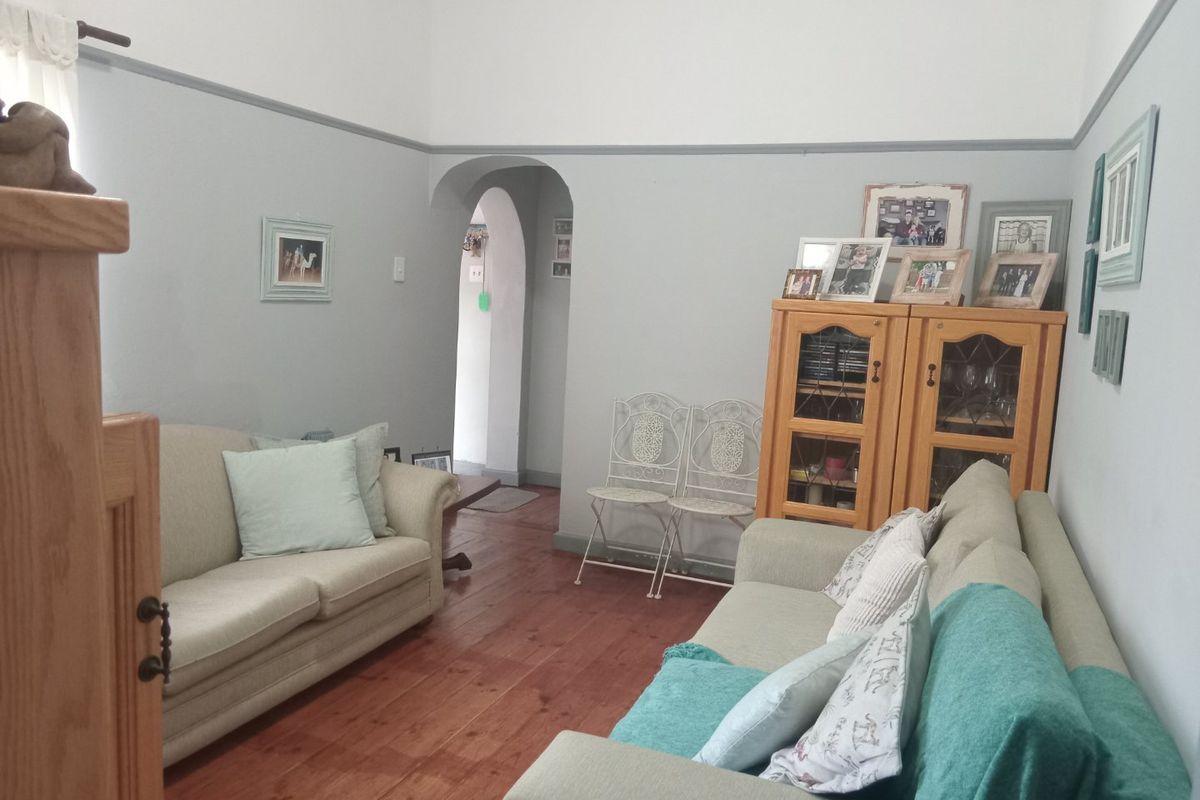A cozy living room featuring original hardwood flooring, a classic archway entrance, and traditional picture rail detailing.