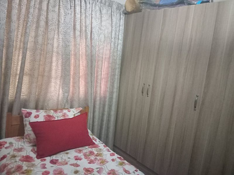 A bedroom featuring a large, wood-finish built-in wardrobe and window curtains.