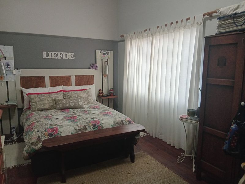 A cozy bedroom featuring timber flooring, high ceilings with a picture rail, and large windows dressed with curtains.
