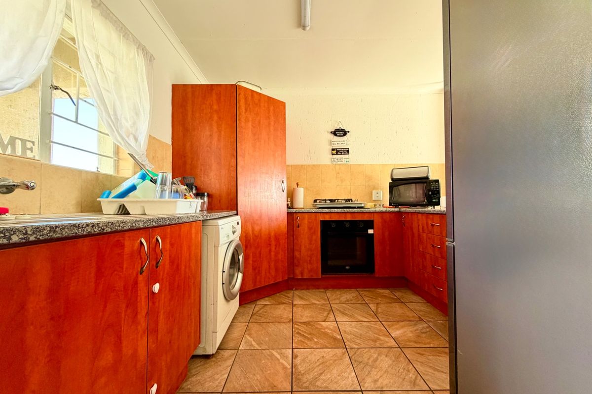 Functional kitchen featuring wood-look cabinetry, granite countertops, built-in oven, gas hob, and tiled flooring with integrated laundry appliance space.