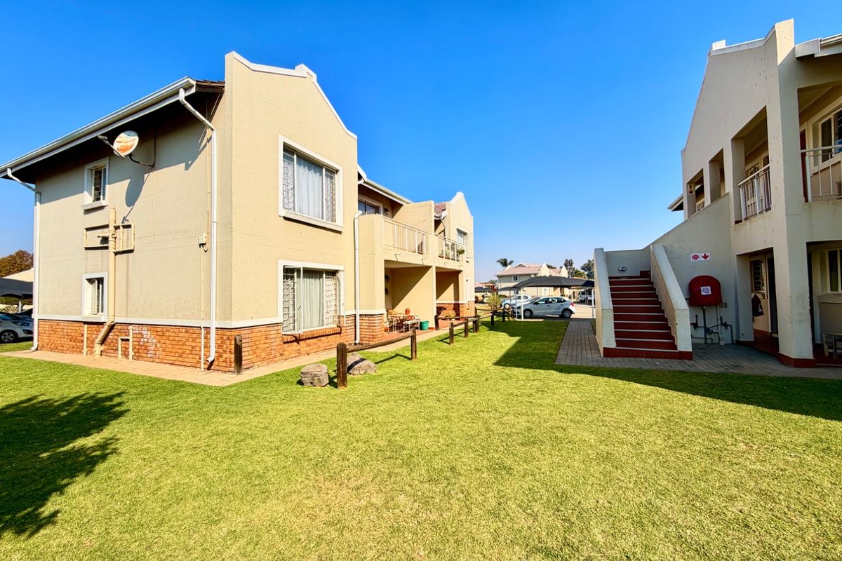 A view of the townhouse complex exterior featuring a shared lawn, paved walkways, external staircases, and balcony access.