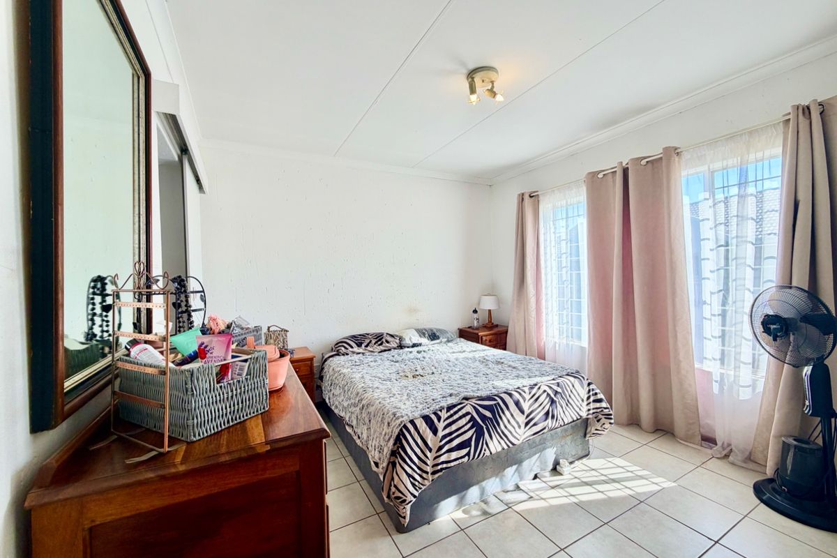 A bedroom featuring tiled flooring and natural light through a window with security bars. The walls show signs of wear and staining.