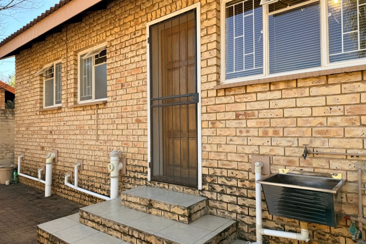 Exterior view of the townhouse rear facade featuring a utility sink, tiled steps, security screen door, and exposed brickwork.