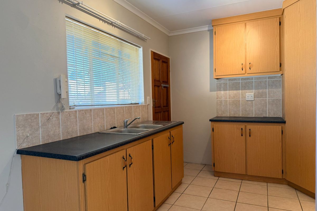 A functional kitchen featuring light wood-finish cabinetry, dark laminate countertops, tiled splashbacks, and ceramic floor tiles.