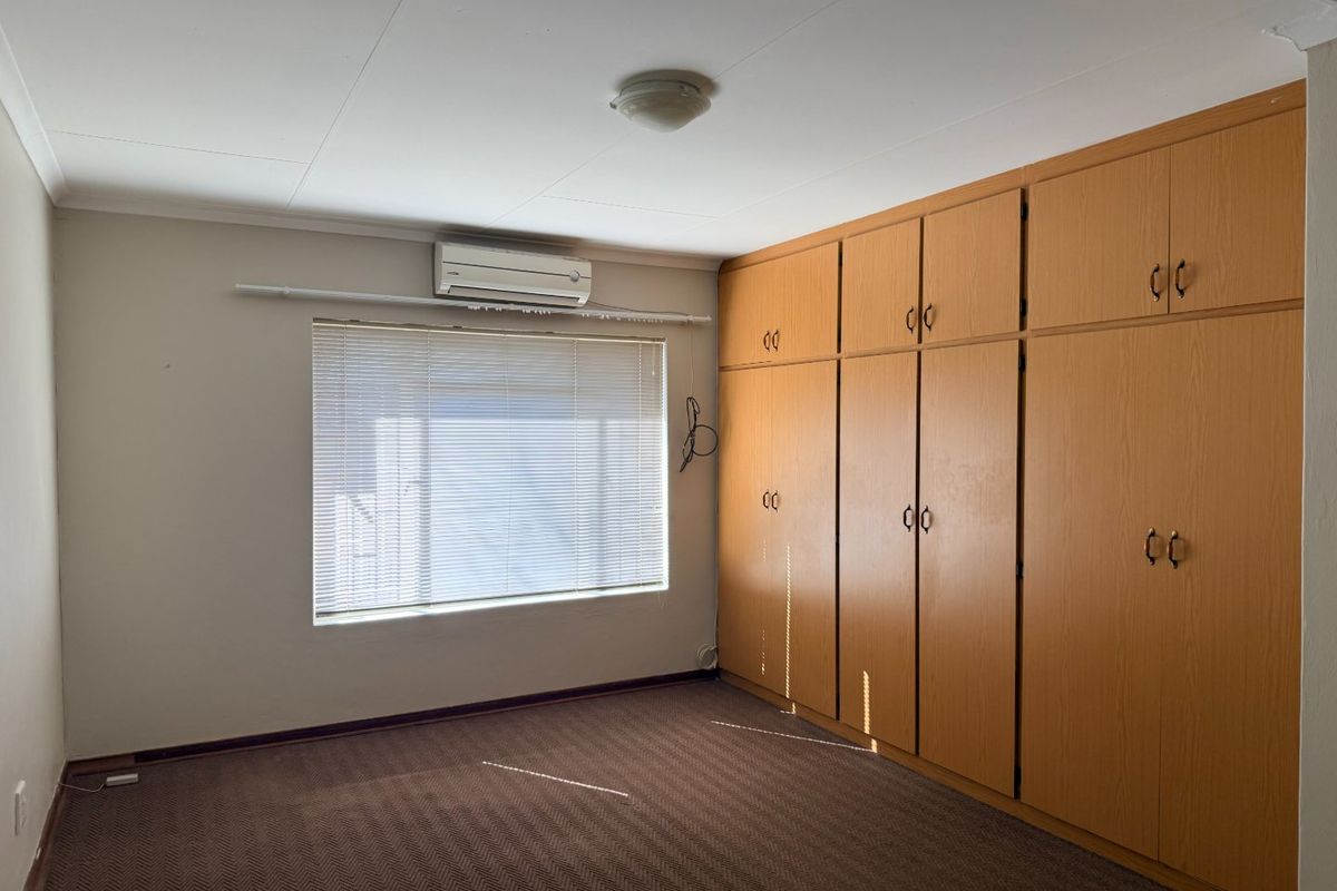 A bedroom featuring built-in wooden cupboards, a wall-mounted air conditioning unit, and carpeted flooring.