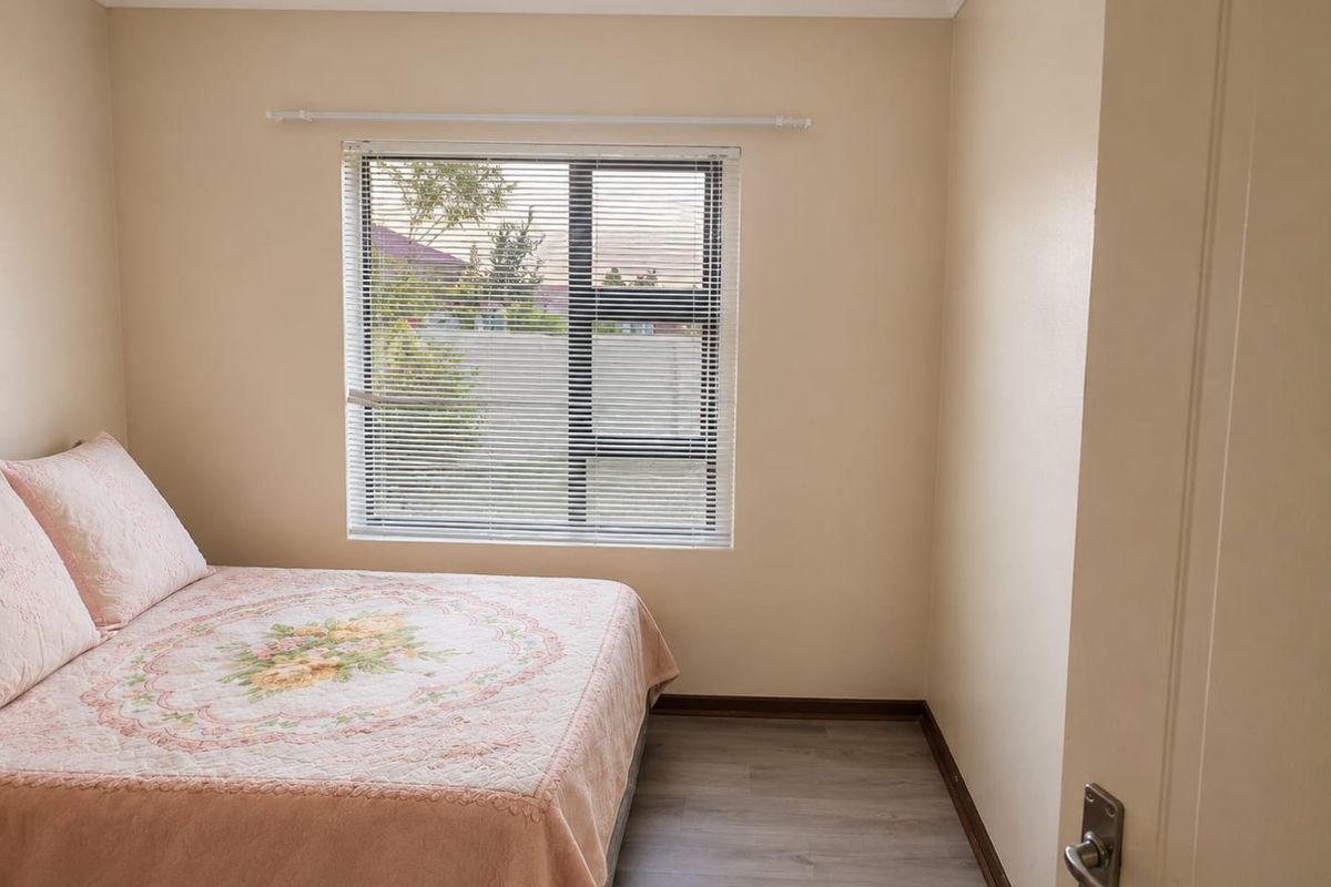 A compact bedroom featuring light-toned walls, wood-look laminate flooring, and a window fitted with horizontal blinds.