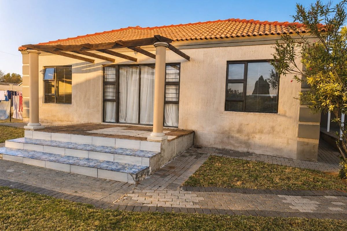 Rear view of a townhouse featuring a covered patio with a pergola, tiled steps, and a paved walkway leading to the garden.
