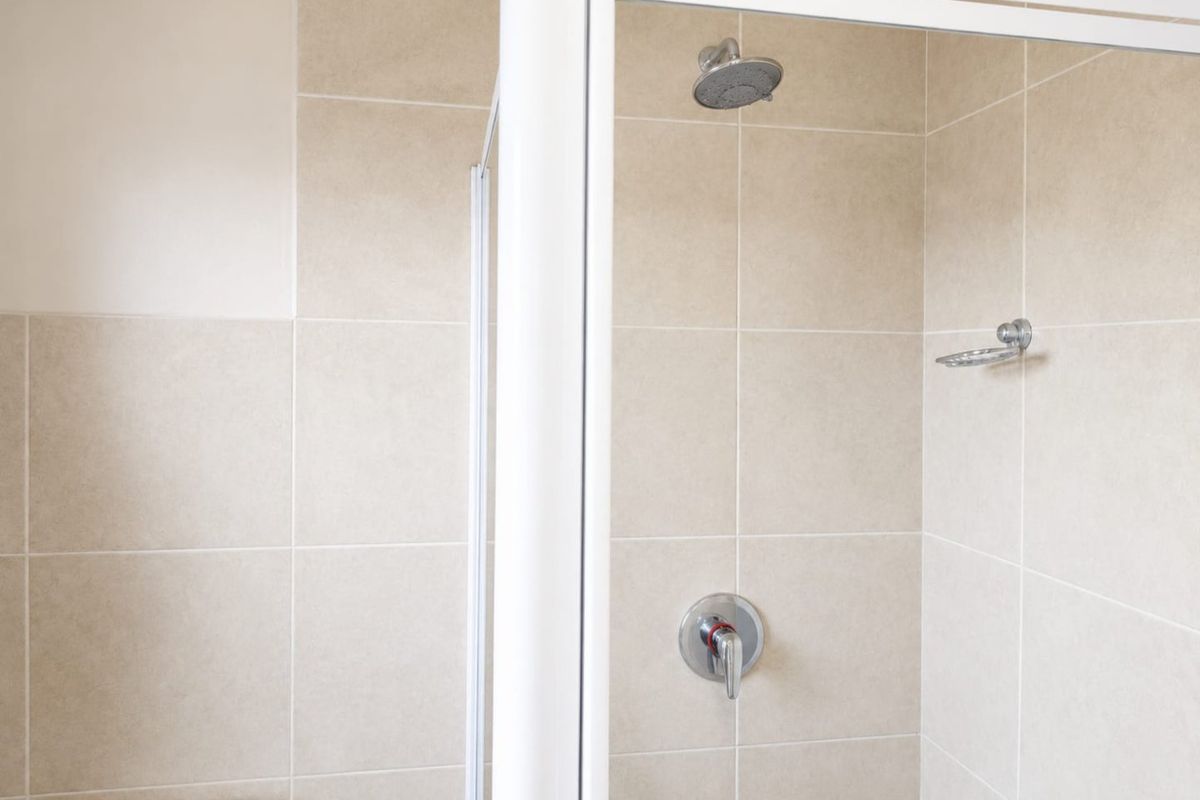 A functional bathroom featuring a tiled shower enclosure with a chrome mixer, shower head, and built-in soap dish.