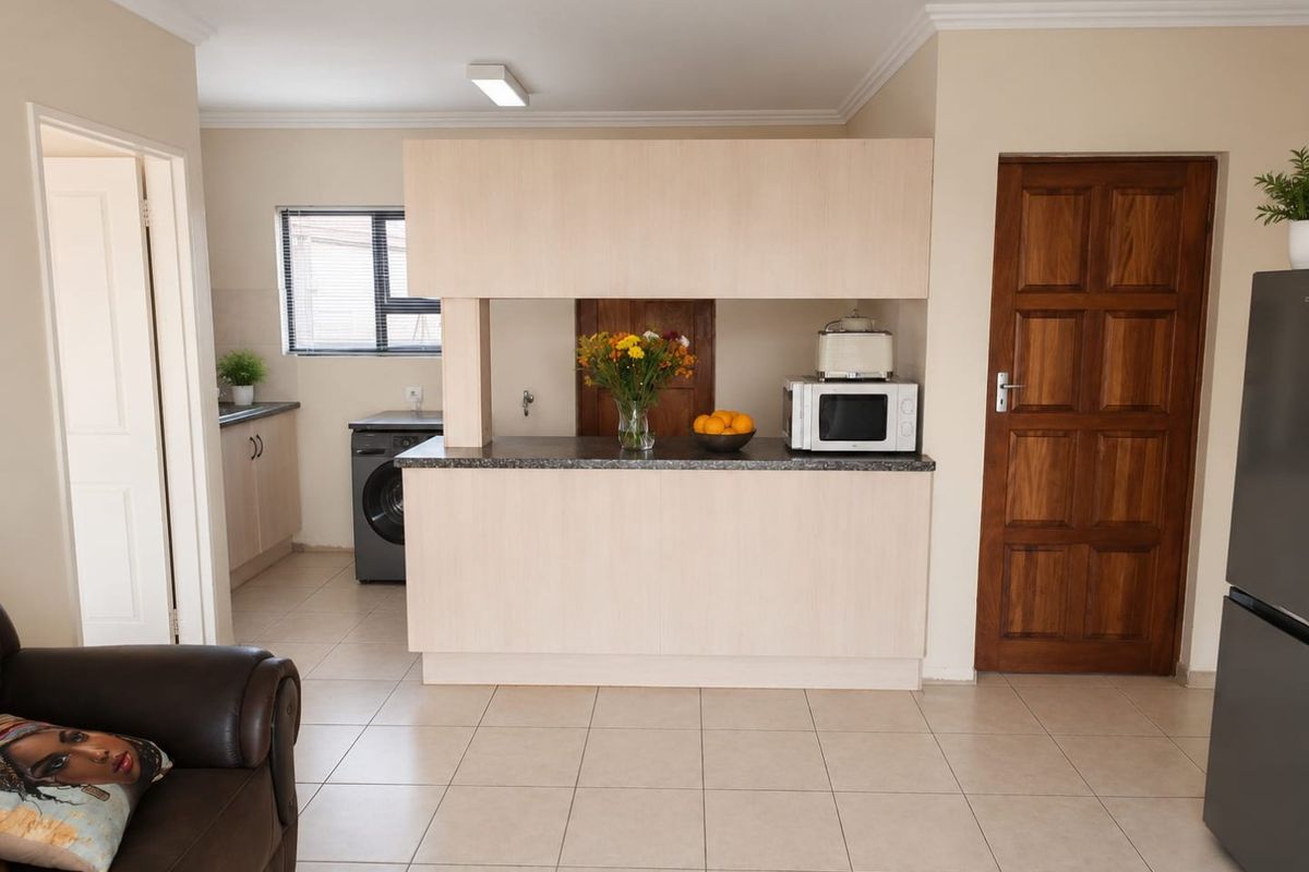 A functional kitchen area featuring light wood cabinetry, a breakfast bar, tiled flooring, and a separate scullery or laundry nook.