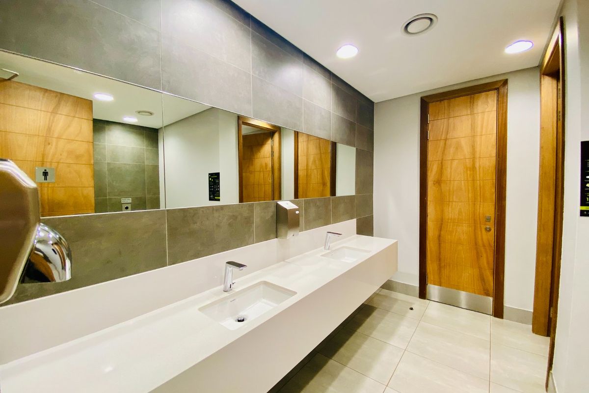 Modern commercial restroom featuring a sleek dual-basin vanity with integrated sinks, large wall-mounted mirrors, and contemporary tiled finishes.