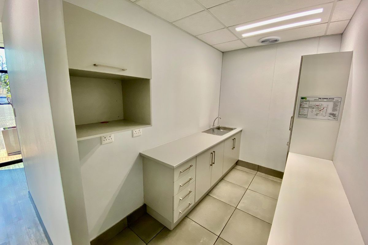 A functional commercial kitchenette featuring built-in cabinetry, a stainless steel sink, tiled flooring, and a suspended ceiling with integrated lighting.