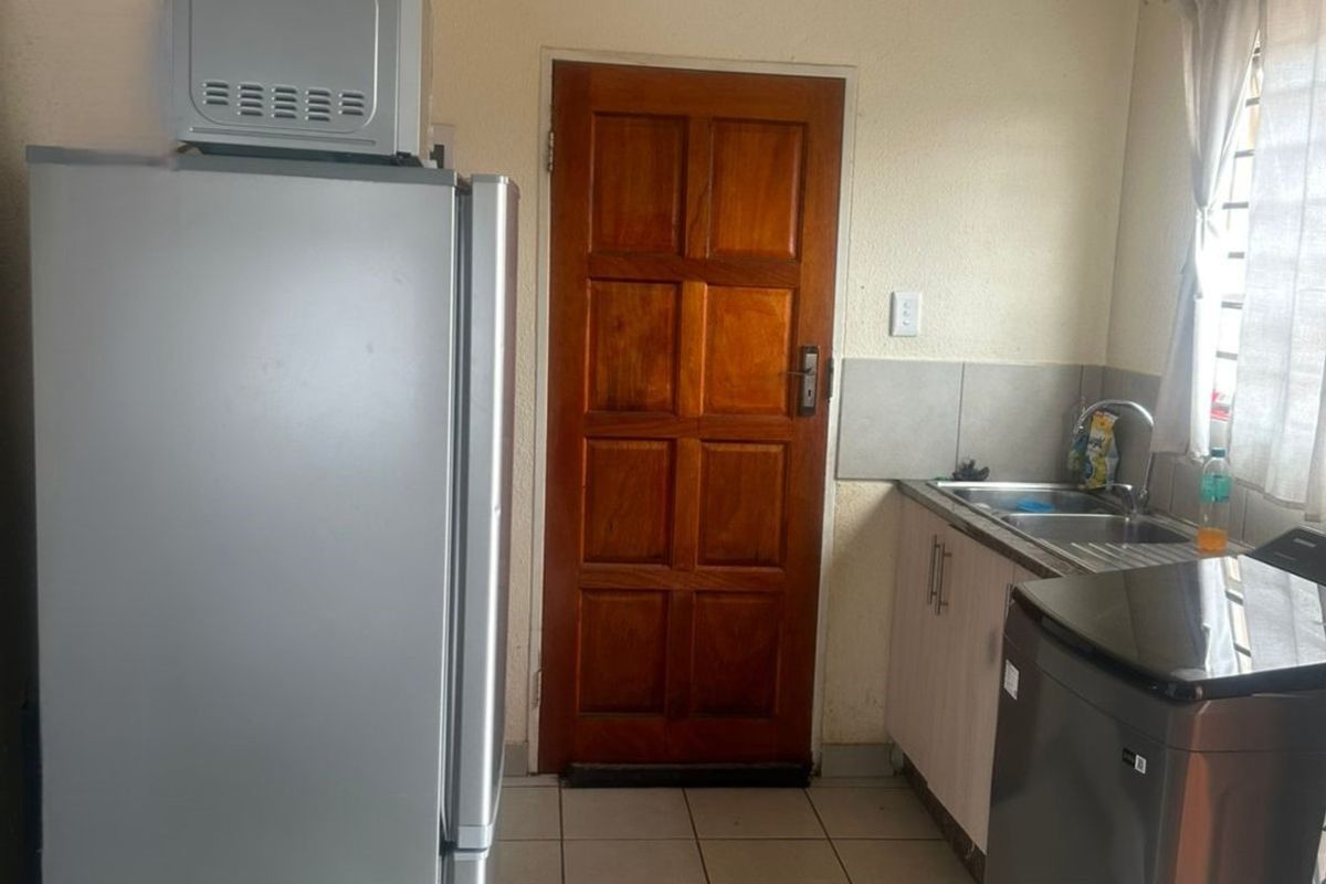 A functional kitchen area featuring tiled flooring, built-in cabinetry with a stainless steel sink, and a solid timber door leading to the exterior.