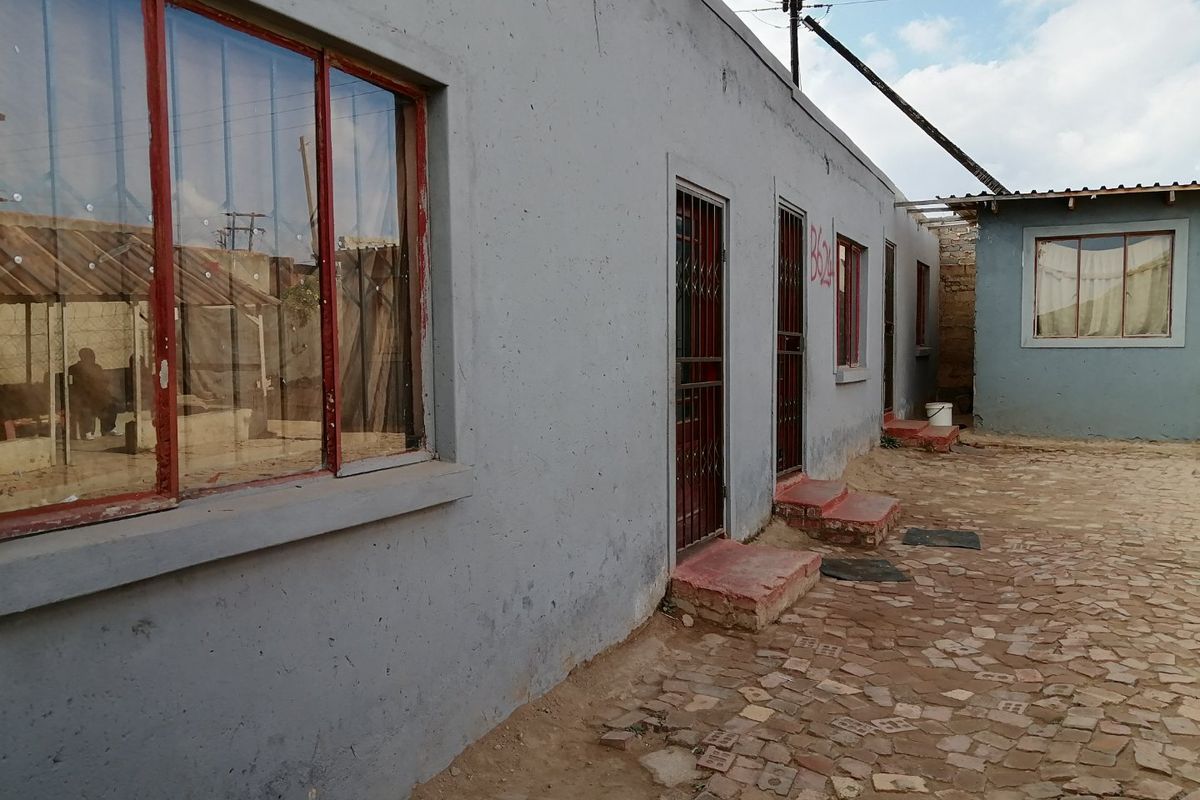 Exterior view of a residential building featuring a paved courtyard, metal security gates, and painted window frames.
