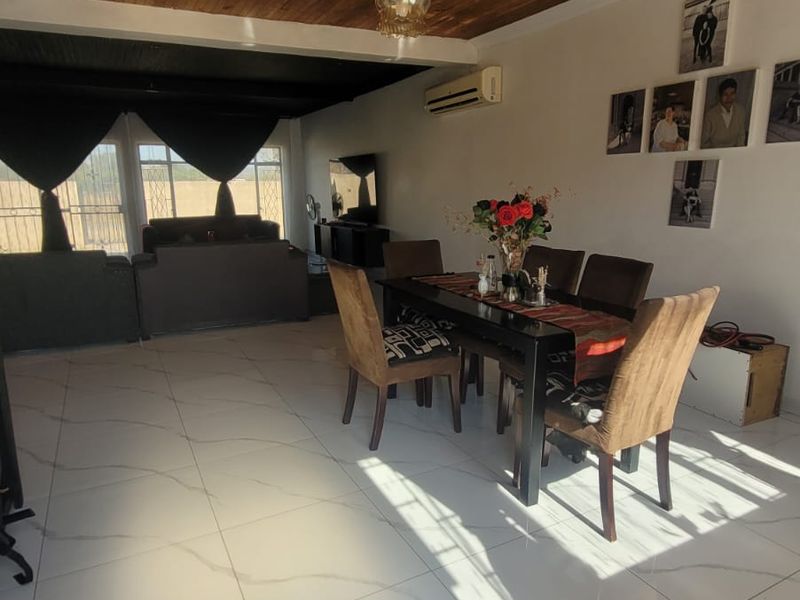 Open plan living and dining area featuring large format floor tiles, a distinctive timber-clad ceiling, and a wall-mounted air conditioning unit.