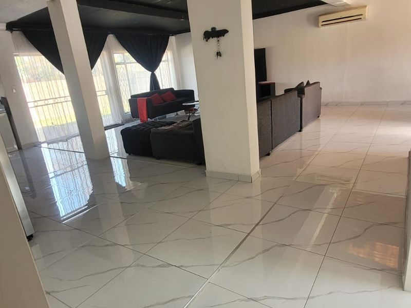 Spacious open-plan living area featuring large format white floor tiles, structural support columns, and a wall-mounted air conditioning unit.