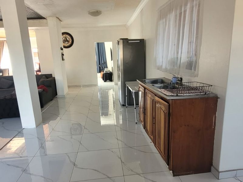 Open plan living area featuring large format marble-look floor tiles and a compact kitchenette unit with a stainless steel sink.