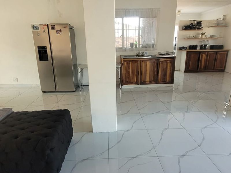Open plan living and kitchen area featuring large format marble-look floor tiles and wooden cabinetry.
