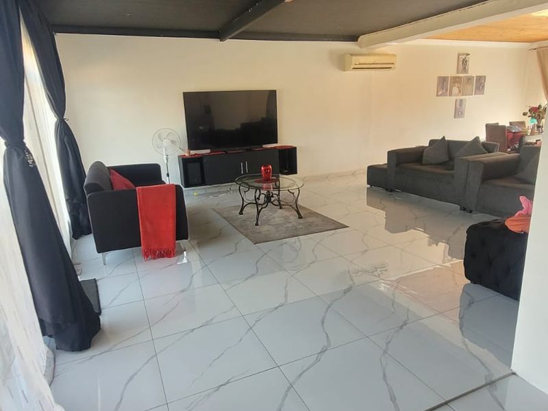Spacious open-plan living area featuring large format marble-look floor tiles, a dark timber-clad ceiling, and a wall-mounted air conditioning unit.