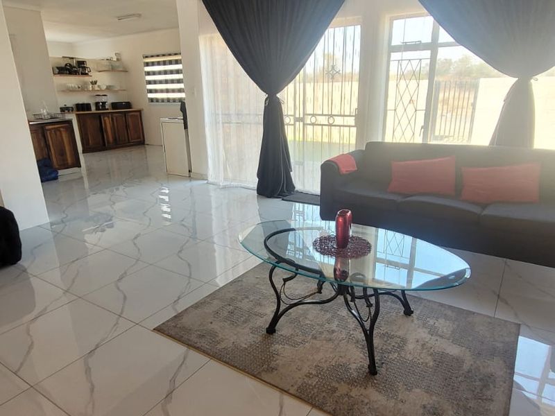 Open-plan living area featuring large format marble-look floor tiles, dark timber-clad ceiling, and direct access to the exterior through sliding glass doors.