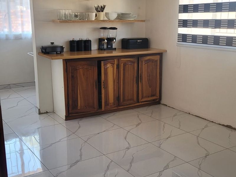 A kitchen area featuring wooden cabinetry, open shelving, and modern marble-look floor tiles with a window fitted with a striped roller blind.