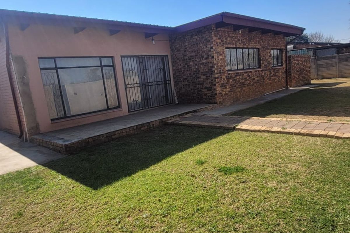Rear view of the house featuring a brick and plastered facade, paved patio area, and a spacious garden lawn.