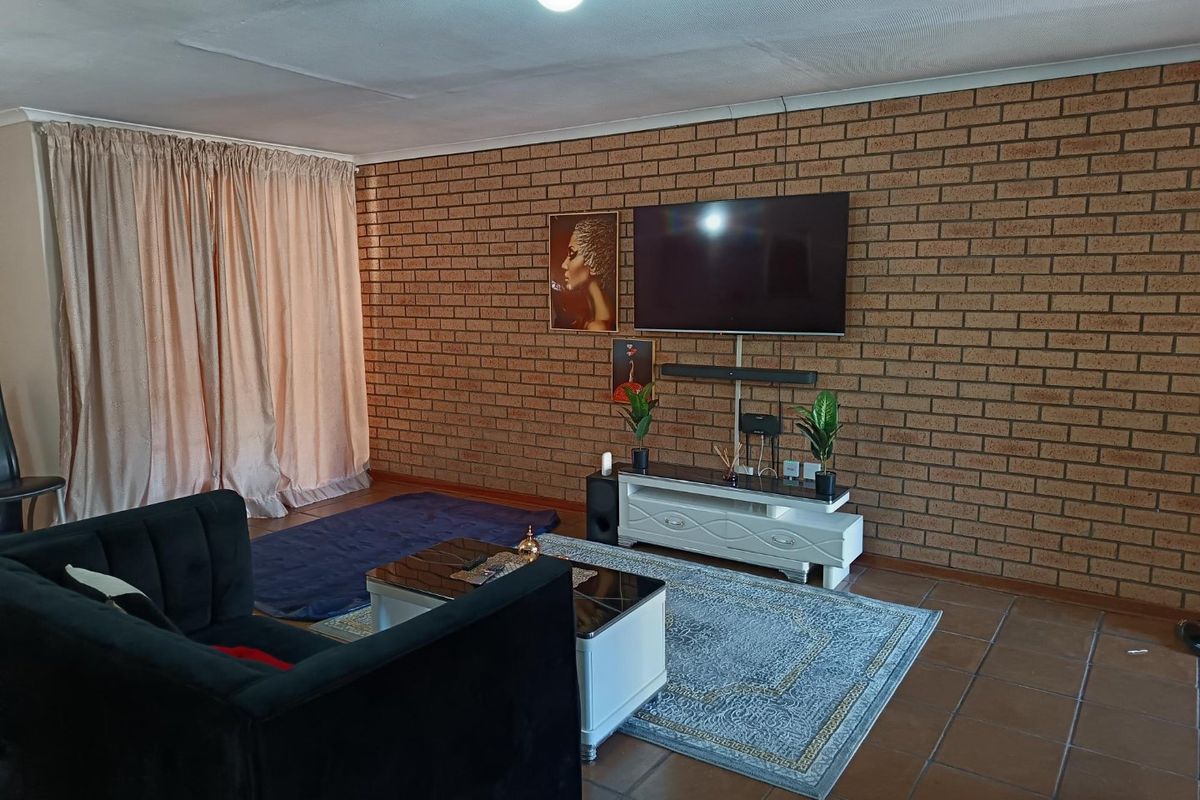 A living room featuring a prominent face-brick feature wall, tiled flooring, and large window coverage.