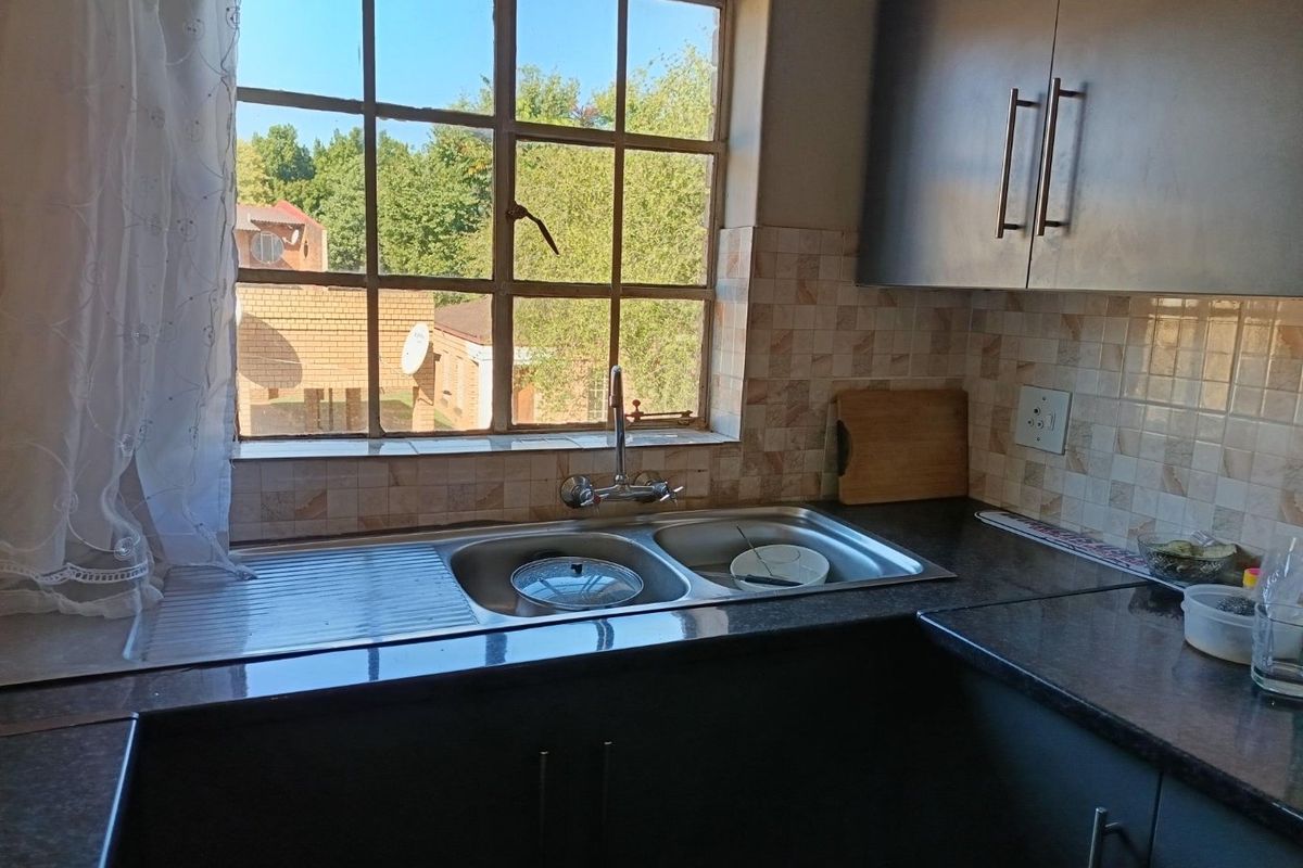 A functional kitchen area featuring dark cabinetry, a double-basin stainless steel sink, and tiled splashbacks with a window overlooking the exterior.