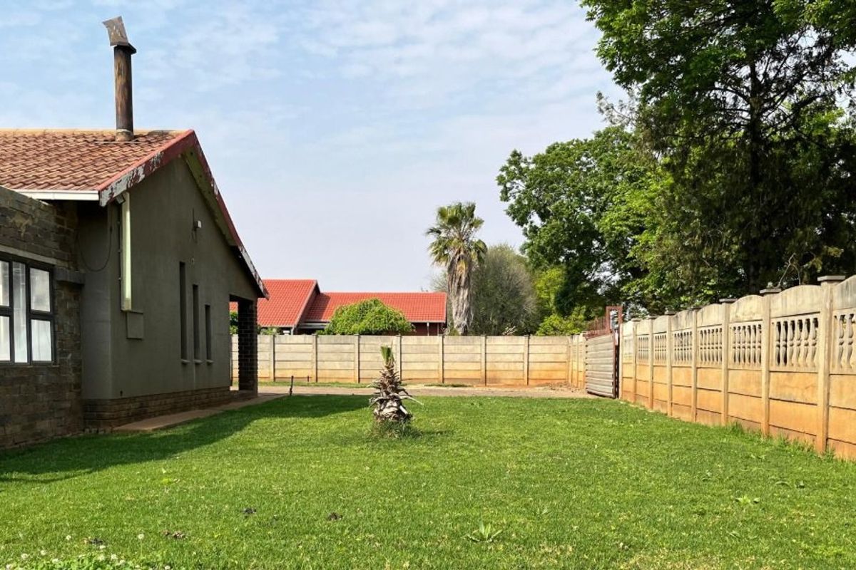 A view of the rear garden featuring a lawn area, perimeter precast concrete walling, and the side elevation of the house with a chimney.