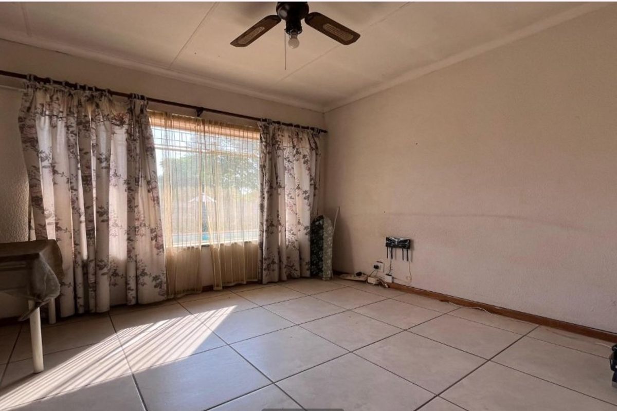 A living room featuring large windows with security bars, tiled flooring, and a ceiling fan, offering a blank canvas for renovation.