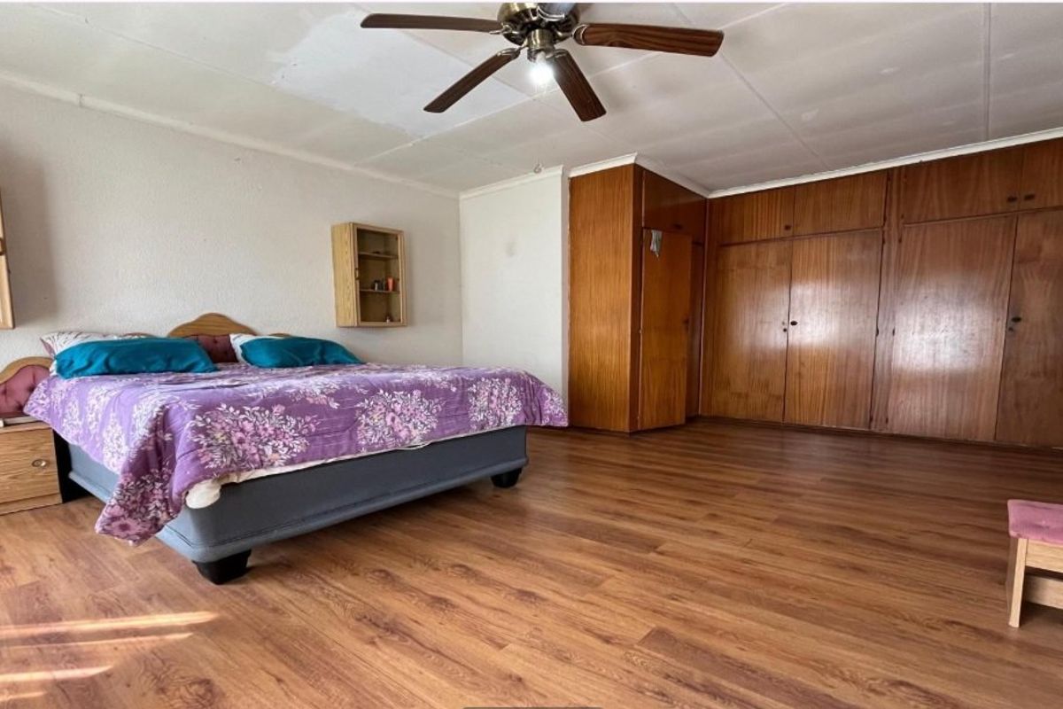 Spacious bedroom featuring built-in wooden wardrobes, laminate flooring, and a ceiling fan, offering a functional layout with potential for modernization.