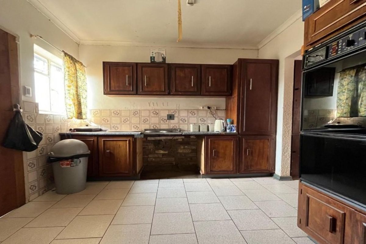 A dated kitchen featuring dark wood cabinetry, tiled flooring, a tiled backsplash, and a built-in double oven.