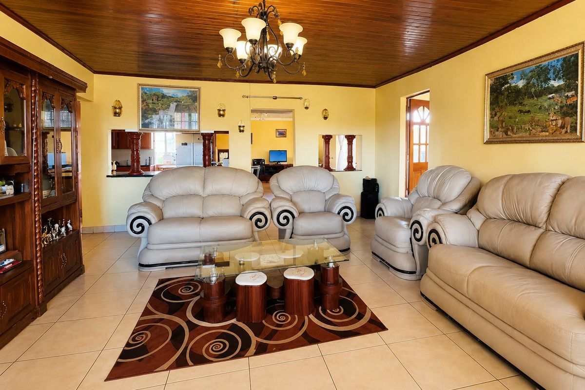 Spacious living room featuring tiled flooring, a timber-paneled ceiling, and a decorative chandelier, with an open-plan layout connecting to the kitchen area.