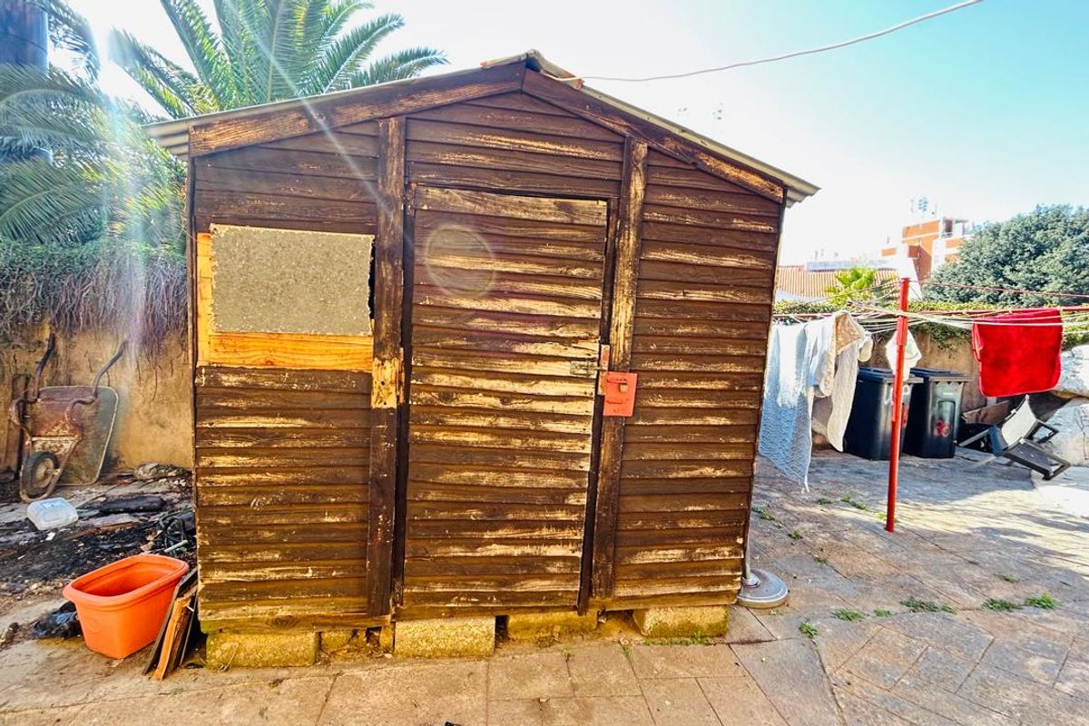 A weathered wooden garden shed located in the rear yard, showing significant signs of wear and requiring maintenance or replacement.
