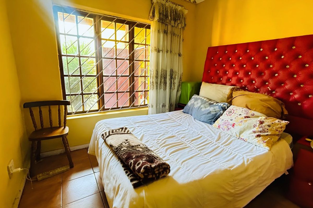 A bedroom featuring tiled flooring, a window with security bars, and a built-in headboard area.