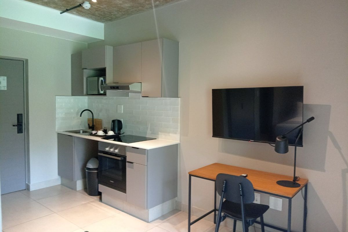 Compact open-plan kitchen featuring modern grey cabinetry, subway tile backsplash, built-in oven, and hob, adjacent to a functional workspace area.