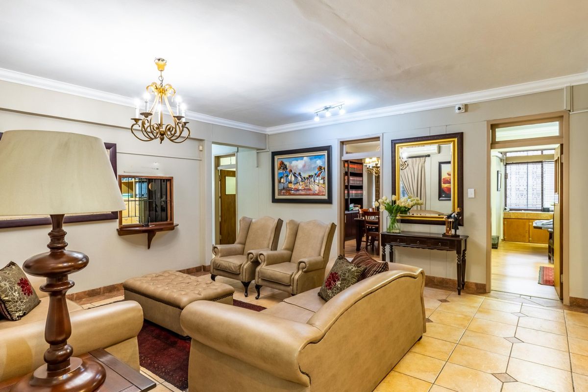 A spacious living area featuring ceramic floor tiles, decorative crown molding, and a classic chandelier, providing a comfortable and well-lit communal space.