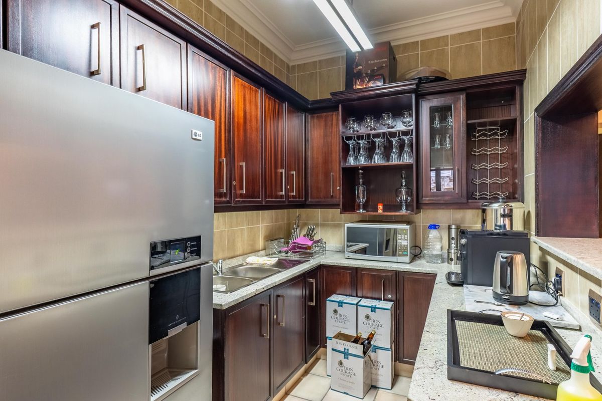 A compact kitchen area featuring dark wood cabinetry, granite countertops, a double basin sink, and tiled wall finishes.