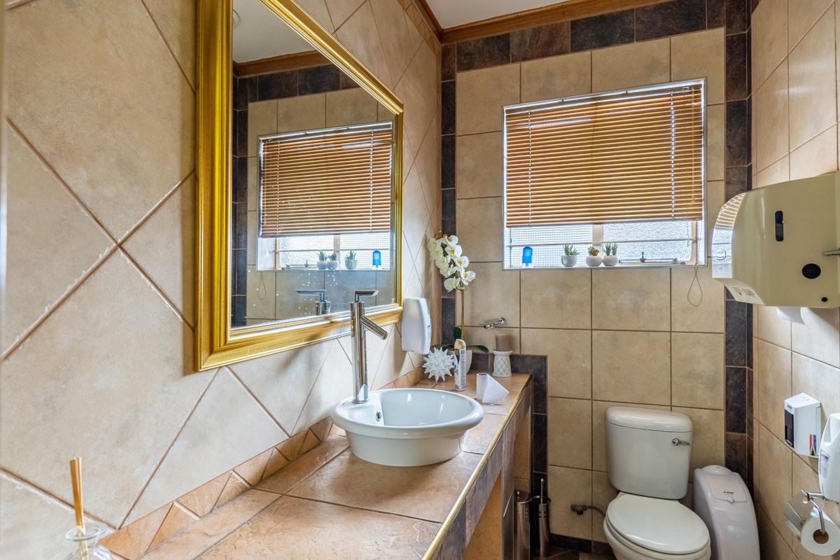 A functional commercial bathroom featuring a vessel sink, wall-mounted mirror, and standard toilet with tiled walls and flooring.