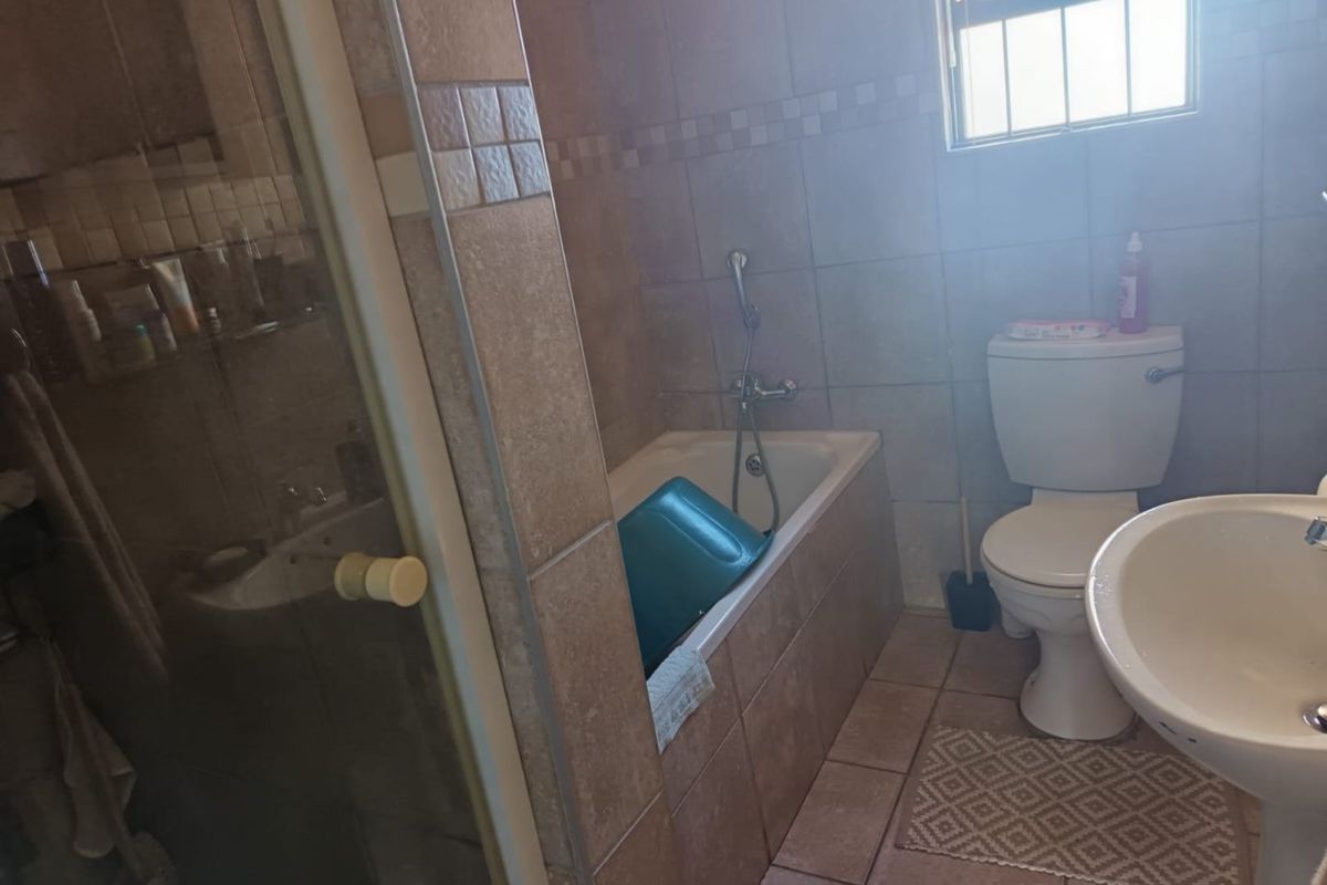 A functional bathroom featuring a tiled bathtub with shower mixer, pedestal basin, and toilet, finished with neutral wall and floor tiles.
