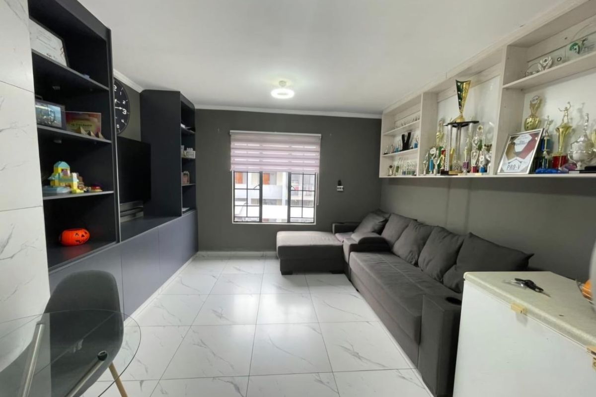 A modern living room featuring built-in dark cabinetry, custom wall-mounted shelving, marble-look floor tiles, and a window with a roller blind.