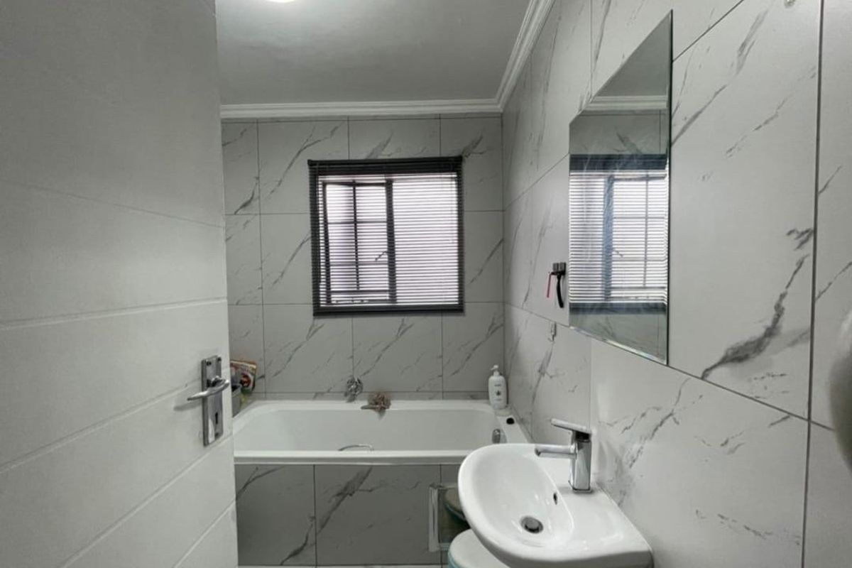 Modern bathroom featuring marble-look wall and floor tiles, a built-in bathtub, pedestal basin, and a wall-mounted mirror.