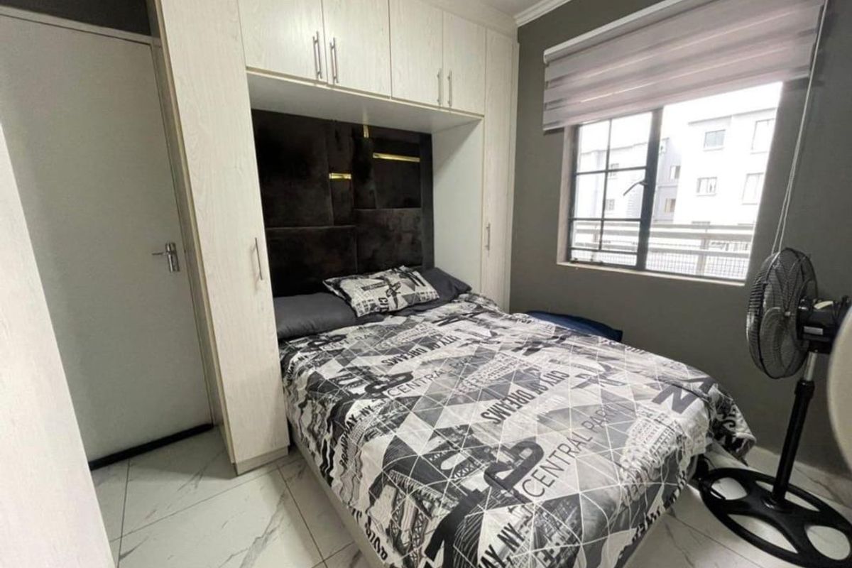 A compact bedroom featuring built-in floor-to-ceiling wardrobes with integrated headboard storage and tiled flooring.