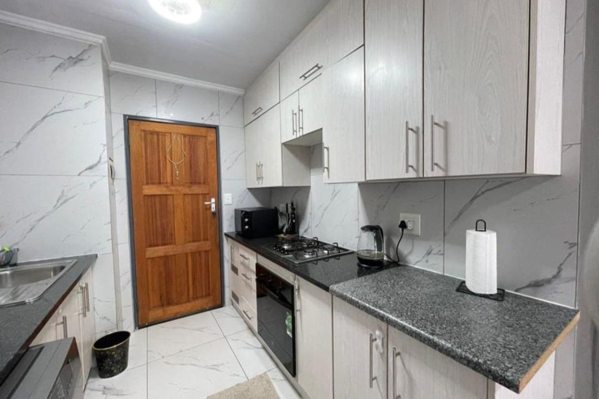 Modern kitchen featuring light wood-grain cabinetry, granite countertops, marble-effect wall tiles, and built-in oven with gas hob.