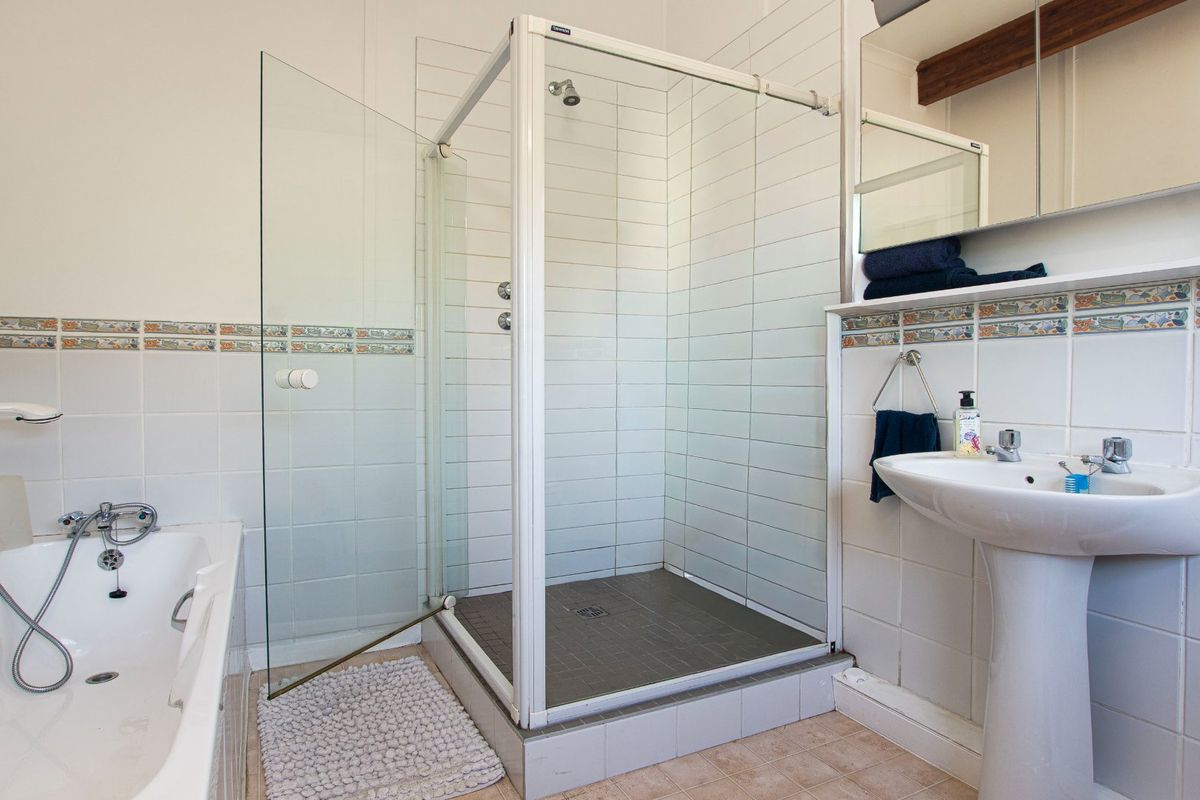 A functional bathroom featuring a separate glass-enclosed shower, a standard bathtub, and a pedestal sink with wall-mounted mirror cabinetry.